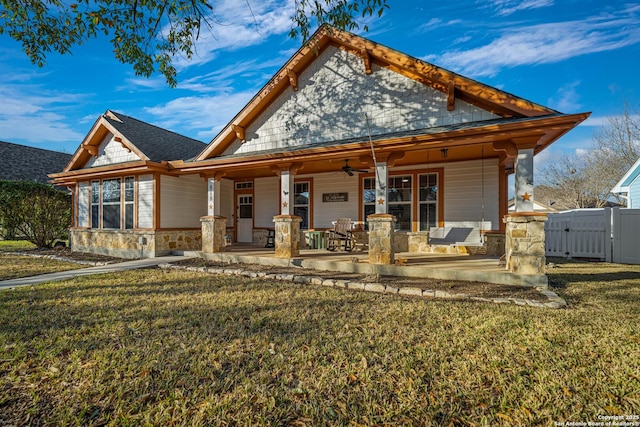 back of property featuring fence, a ceiling fan, a yard, covered porch, and stone siding