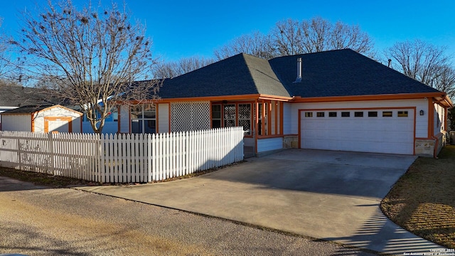 ranch-style house with fence private yard, stone siding, roof with shingles, concrete driveway, and an attached garage