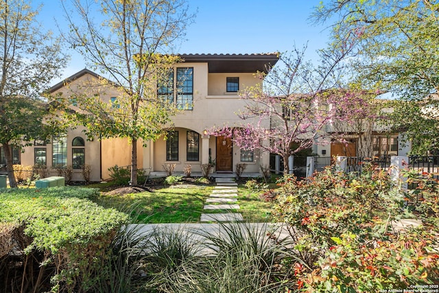 mediterranean / spanish home featuring a tiled roof, stucco siding, a front lawn, and fence