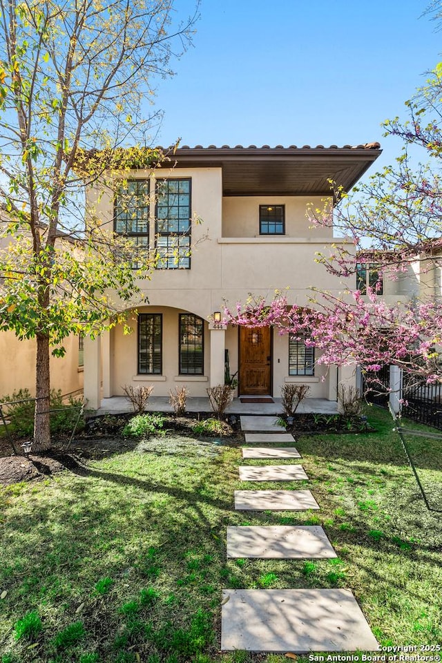 view of front of property featuring stucco siding, fence, a front yard, and a tiled roof