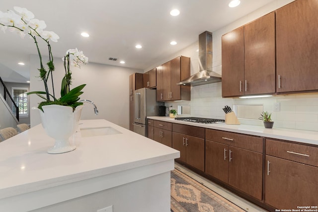 kitchen featuring visible vents, a sink, stainless steel appliances, light countertops, and wall chimney exhaust hood