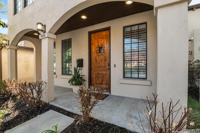 property entrance with stucco siding, a porch, and fence