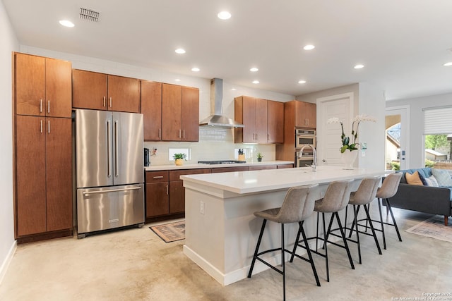 kitchen featuring visible vents, concrete floors, decorative backsplash, stainless steel appliances, and wall chimney exhaust hood