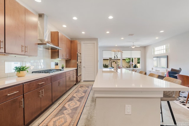 kitchen with tasteful backsplash, wall chimney range hood, a breakfast bar area, light countertops, and stainless steel gas stovetop