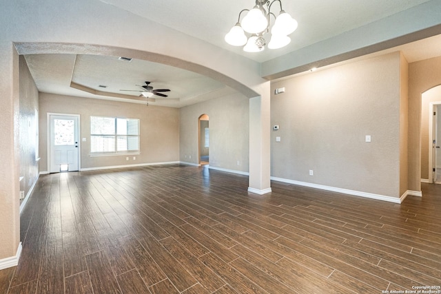 unfurnished living room featuring dark wood finished floors, a raised ceiling, ceiling fan with notable chandelier, and arched walkways