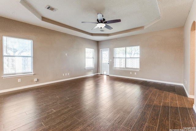 unfurnished room with a tray ceiling, a ceiling fan, dark wood-style flooring, and baseboards