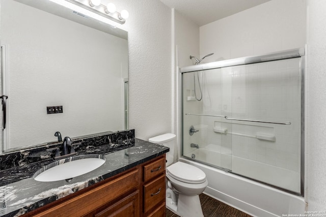 full bathroom with visible vents, toilet, wood finished floors, shower / bath combination with glass door, and vanity