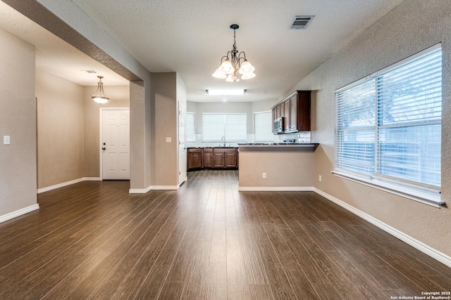 kitchen with visible vents, dark wood-type flooring, baseboards, a chandelier, and a peninsula