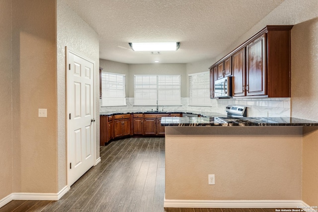 kitchen featuring decorative backsplash, dark wood-style flooring, a peninsula, stainless steel appliances, and a sink