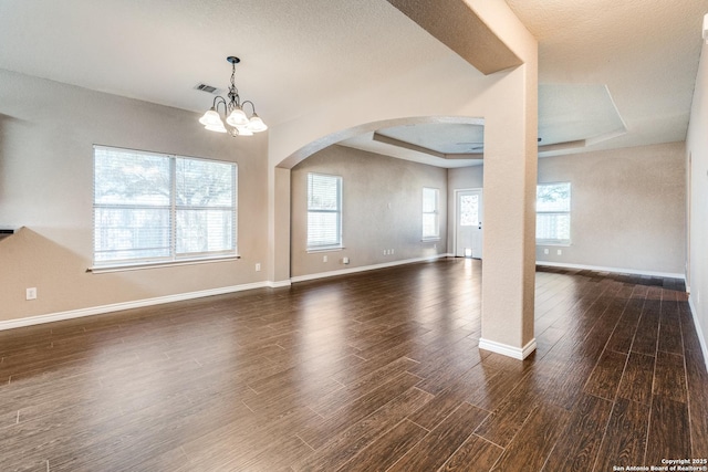 interior space featuring baseboards, arched walkways, a raised ceiling, and dark wood-style floors