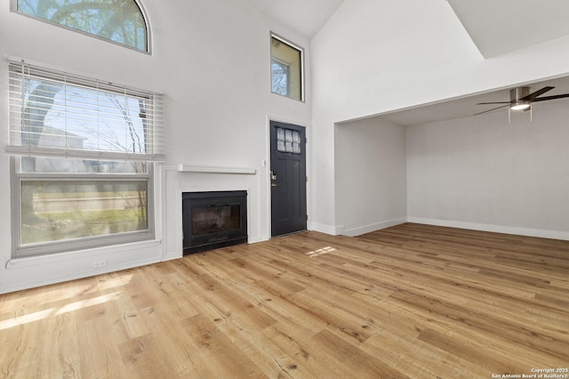 unfurnished living room with a glass covered fireplace, baseboards, hardwood / wood-style floors, and ceiling fan