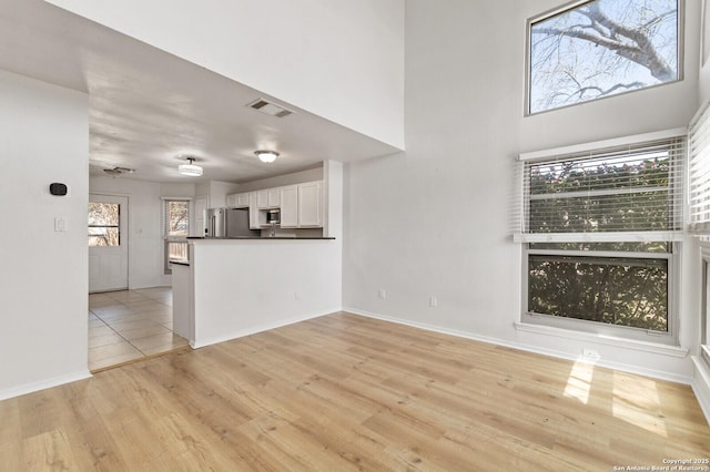 unfurnished living room with visible vents, baseboards, a high ceiling, and light wood finished floors