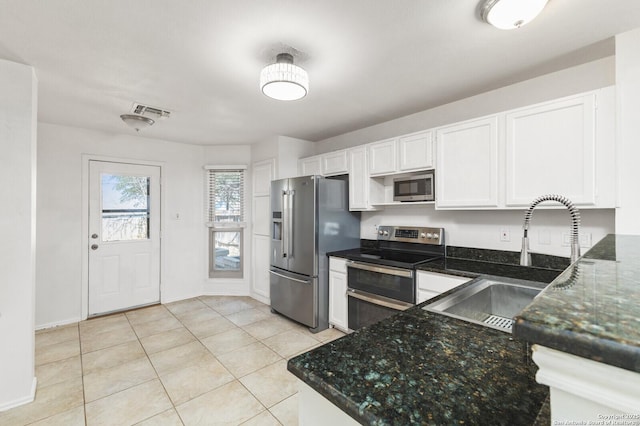 kitchen featuring a sink, dark stone countertops, stainless steel appliances, white cabinets, and light tile patterned floors