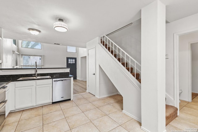 kitchen with dark countertops, dishwasher, light tile patterned floors, white cabinets, and a sink