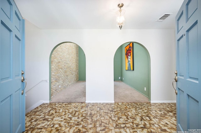 carpeted foyer with visible vents, arched walkways, and baseboards