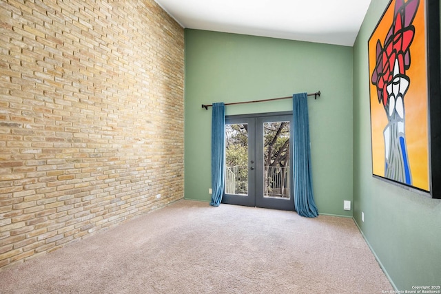 carpeted empty room featuring french doors, brick wall, and a high ceiling