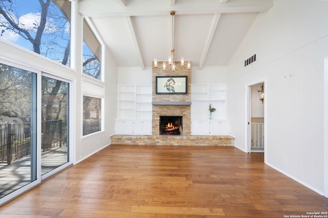 unfurnished living room with a large fireplace, built in shelves, a notable chandelier, and wood finished floors