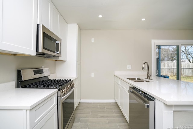 kitchen featuring a sink, appliances with stainless steel finishes, a peninsula, white cabinets, and light countertops