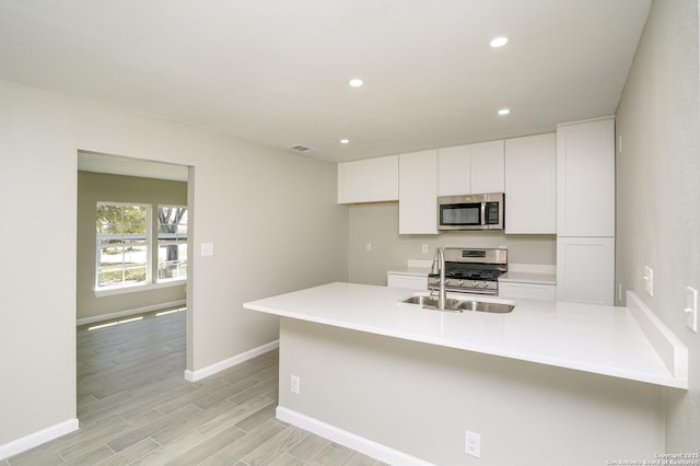 kitchen with recessed lighting, a peninsula, stainless steel appliances, white cabinetry, and a sink