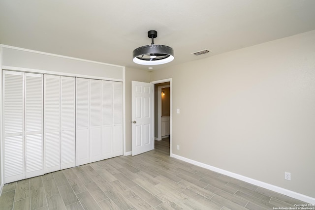 unfurnished bedroom featuring a closet, visible vents, light wood-style flooring, and baseboards