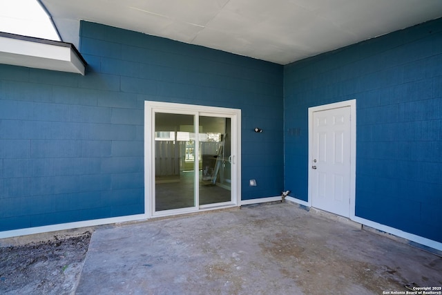 view of exterior entry with concrete block siding and a patio