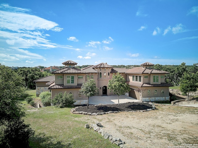 mediterranean / spanish-style house with a tiled roof, a front yard, stucco siding, a patio area, and driveway