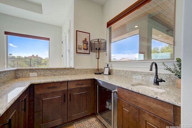 kitchen featuring wine cooler, light stone counters, brick floor, and a sink