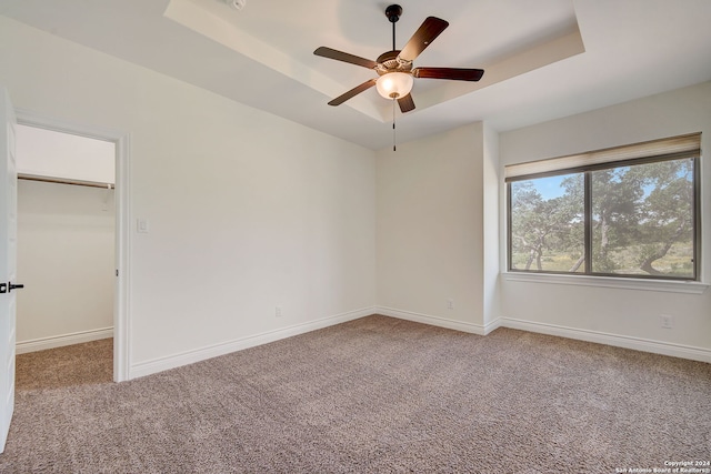 interior space with a walk in closet, baseboards, carpet, a raised ceiling, and a ceiling fan