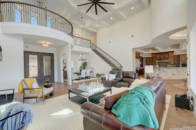 living room featuring beam ceiling, ceiling fan with notable chandelier, coffered ceiling, french doors, and arched walkways