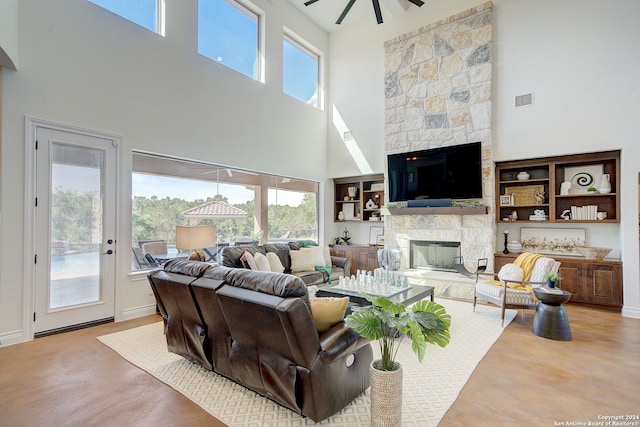 living area with a stone fireplace, a high ceiling, a ceiling fan, and visible vents