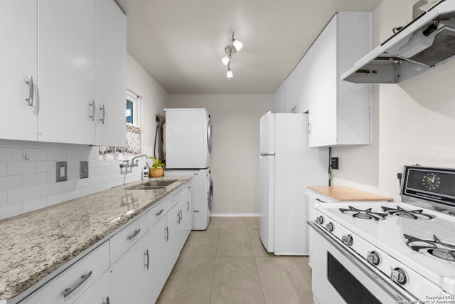 kitchen with backsplash, under cabinet range hood, stacked washer and dryer, white appliances, and a sink