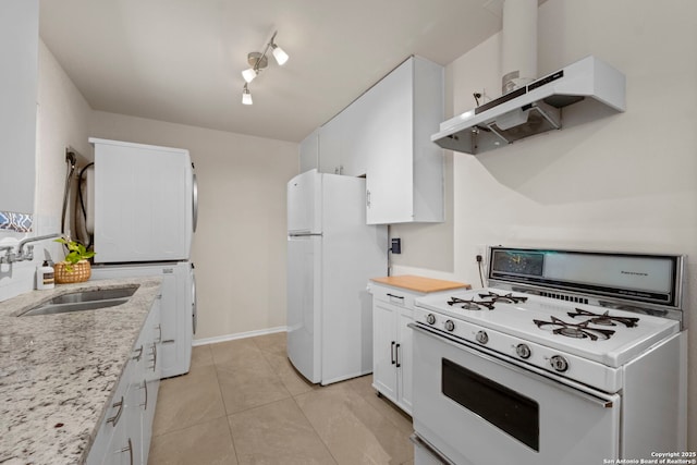 kitchen featuring stacked washer and clothes dryer, a sink, under cabinet range hood, white appliances, and white cabinets