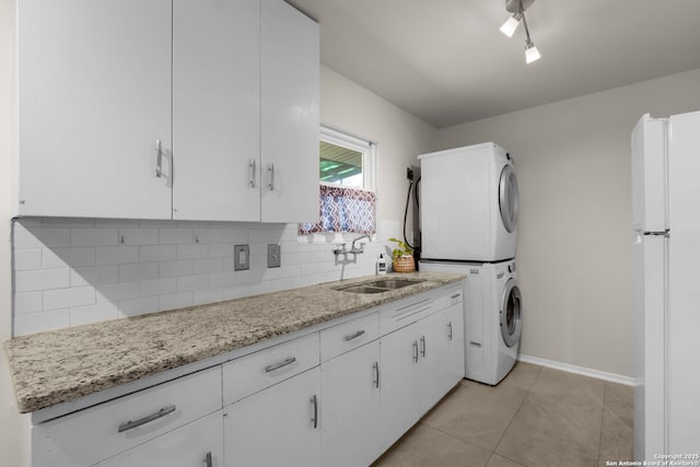 laundry area featuring light tile patterned floors, baseboards, stacked washer and clothes dryer, and a sink