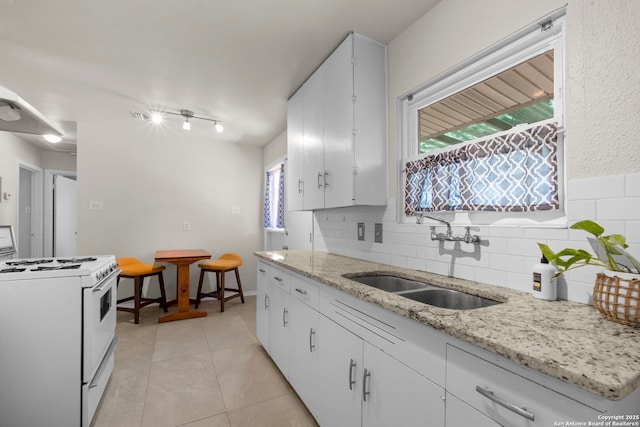 kitchen with light stone counters, light tile patterned floors, white range with gas cooktop, a sink, and tasteful backsplash