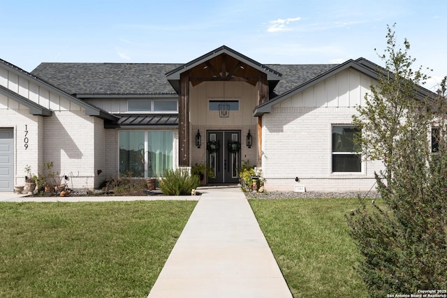 modern inspired farmhouse featuring french doors, brick siding, roof with shingles, and a front lawn