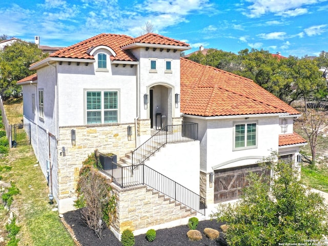 mediterranean / spanish-style home featuring a tile roof, fence, stone siding, and stucco siding