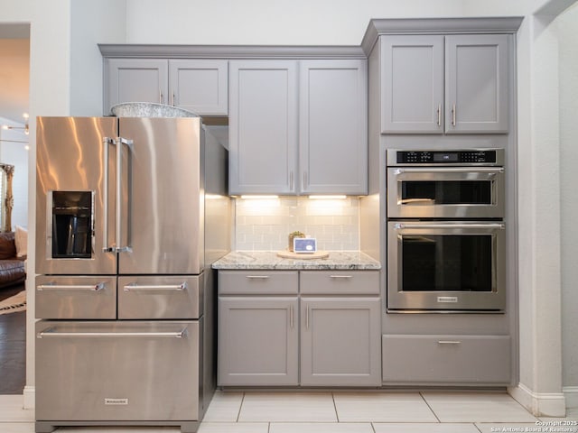 kitchen featuring light stone counters, backsplash, appliances with stainless steel finishes, and gray cabinets