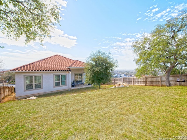 rear view of house with a lawn, a fenced backyard, and a tile roof