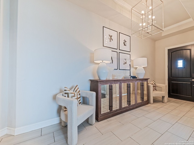 entrance foyer with baseboards, a notable chandelier, a raised ceiling, and crown molding