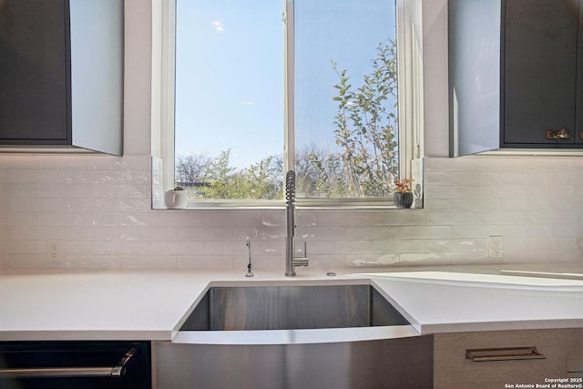 kitchen with dishwasher, light countertops, tasteful backsplash, and a sink