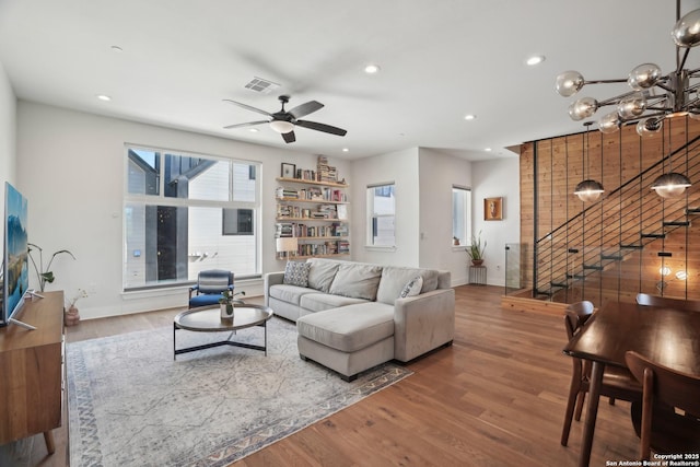 living room featuring visible vents, stairs, recessed lighting, ceiling fan with notable chandelier, and wood finished floors