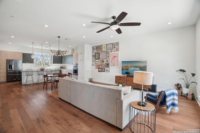 living area featuring dark wood-type flooring, recessed lighting, and ceiling fan with notable chandelier