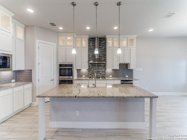 kitchen with white cabinetry, wall chimney range hood, visible vents, and appliances with stainless steel finishes