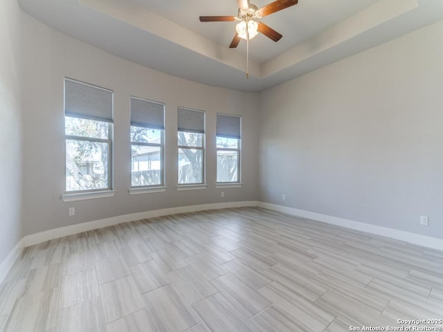 unfurnished room with light wood-style floors, a raised ceiling, a ceiling fan, and baseboards