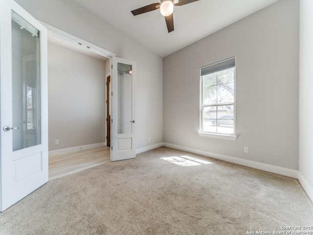 carpeted spare room with vaulted ceiling, french doors, baseboards, and ceiling fan