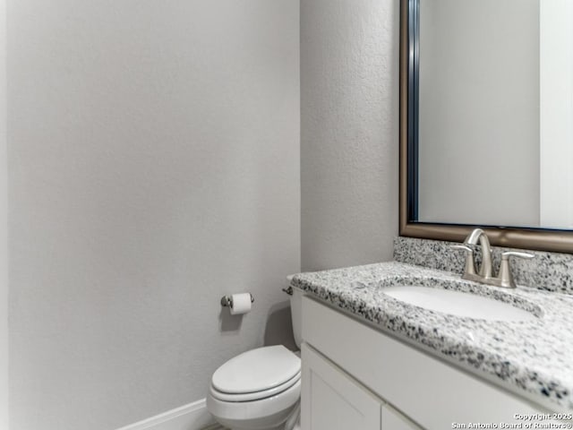 half bath with baseboards, toilet, and vanity