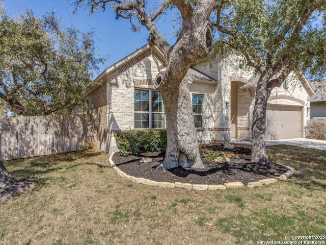 view of front of house with a front yard, fence, driveway, an attached garage, and stone siding