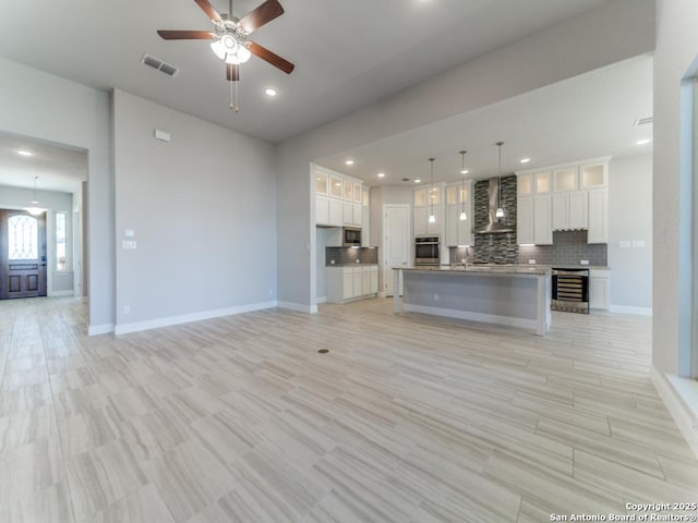 unfurnished living room with beverage cooler, a ceiling fan, visible vents, baseboards, and recessed lighting