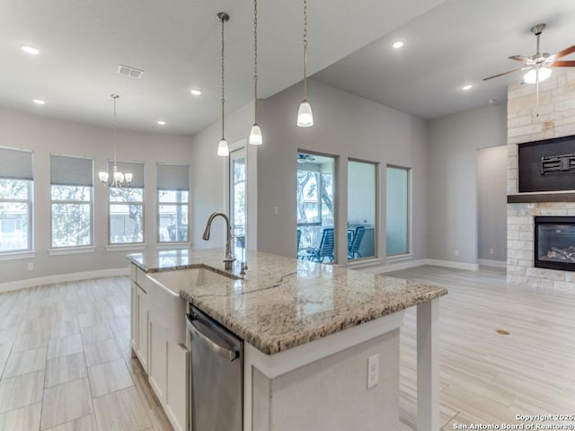 kitchen with visible vents, a sink, a stone fireplace, stainless steel dishwasher, and open floor plan