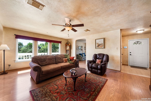 living area featuring visible vents, wood finished floors, arched walkways, a textured ceiling, and a ceiling fan